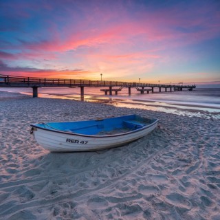 Pier on the fine sandy beach of the Baltic Sea at sunset, fishing boat on the beach, Baltic resort