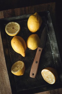 A rustic kitchen scene with fresh lemons on a vintage metal tray, accompanied by a wooden handled