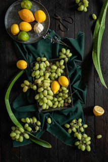 A vibrant display of green grapes, lemons, and limes on a dark wooden surface. The contrasting