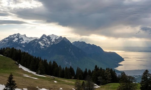 Snow-capped alpine peaks frame Lake Geneva under a dramatic cloudy sky Sunlight casts golden hues