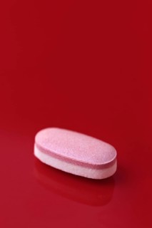 A single pink tablet placed centrally on a vivid red background, conveying a bold contrast that
