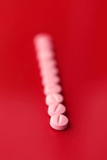 A series of pink medicine tablets aligned diagonally against a stark red background, providing a