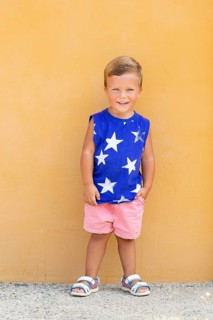 A cheerful young boy in a blue shirt with white stars poses against a vibrant yellow wall His pink