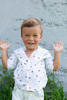 A cheerful child with an adorable smile raises their hands playfully against a textured wall