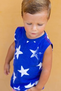 A young child wearing a blue shirt with white star patterns stands against a light orange wall The