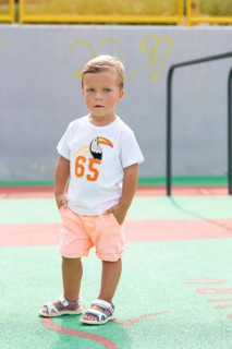 A young boy stands confidently on a vibrant playground, wearing a white T-shirt and peach shorts