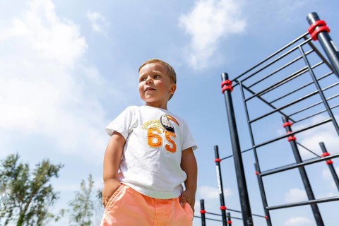 A young child stands confidently in a playground, wearing a colorful outfit against a clear blue