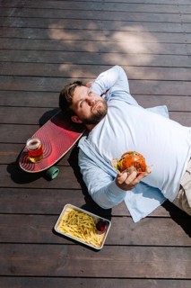 A person enjoying a relaxing moment on a wooden deck, holding a burger. Nearby, there's a