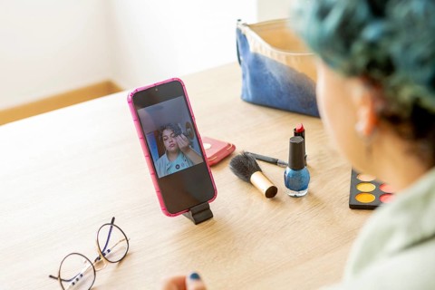 A transgender man records a makeup tutorial with his mobile phone, showcasing various cosmetic