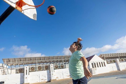 Teenager with Down syndrome playing basketball outdoors, emphasizing sports, captured in an open