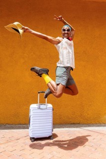 A joyful LGBTQIA+ man jumps exuberantly with a suitcase, ready to embark on a vibrant holiday trip.