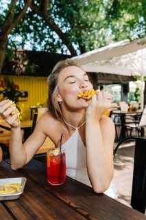 A woman at an outdoor barbecue enjoys a plate of crispy fries and a refreshing drink. Sunlight