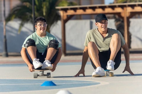 A Down syndrome teenager and his brother practice sports together, enjoying skateboarding outdoors