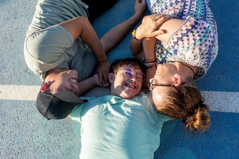 A teenager with Down Syndrome lying outdoors with family, enjoying a loving and joyful moment