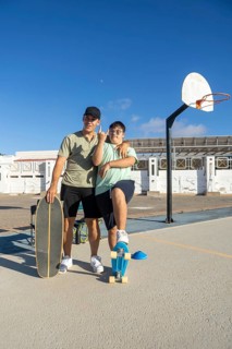 A teenager with Down Syndrome poses confidently with his brother and skateboards on an outdoor