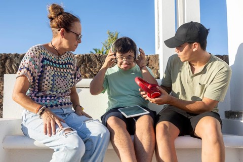 A teenager with Down Syndrome interacting with family outdoors while wearing headphones and holding