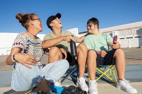 Down syndrome teenager sits with family members, sharing laughter and joy during an outdoor sports