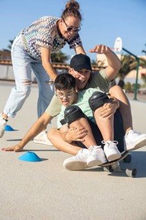 A Down syndrome teenager enjoys a playful skateboard ride with family support in an outdoor setting