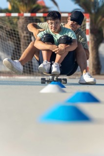A teenager with Down syndrome enjoys a sporting activity with his brother, riding a skateboard