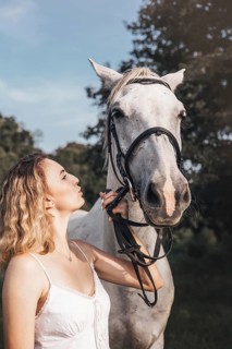 A young woman in a white dress shares a serene moment with a white horse outdoors. The sunlight
