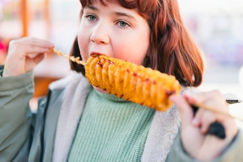 A young girl enjoys a spiral tornado potato on a stick outdoors. The crispy, golden snack is