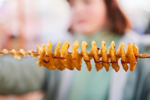 Close-up of golden-brown spiral tornado potatoes on a skewer, drizzled with savory sauce. This