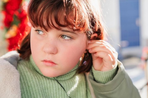 Close-up of a young girl adjusting her headphones, highlighting a thoughtful expression with a soft