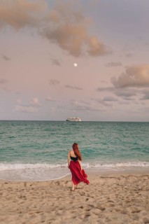 Back view of an unrecognizable redhead woman strolling along Miami Beach. She wears a flowing red