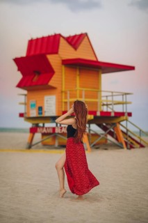 Back view of unrecognizable redhead woman walking near a vividly colored lifeguard station on Miami