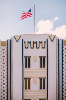 A vibrant American flag waves above a pastel Art Deco building under a clear blue sky, capturing