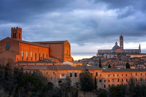 A stunning view of Siena at sunset, featuring the illuminated San Domenico Basilica and the Siena