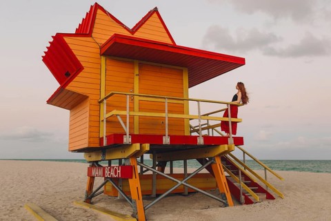 A redhead woman enjoys a quiet moment on the stairs of an iconic orange and red lifeguard station