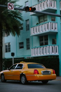 A bright yellow taxi cab parked on a palm-lined street in Miami with a multi-story turquoise