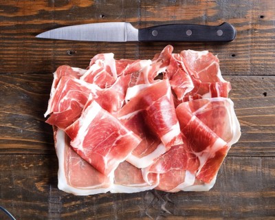 Thinly sliced cured ham arranged on a wooden board beside a sharp kitchen knife, highlighting the
