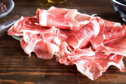 Thin, delicately rolled slices of fresh ham displayed on a dark wooden surface, highlighted by