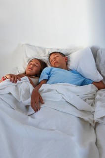 A young girl and boy, are captured sleeping peacefully side by side in a bright, cozy bed setting,