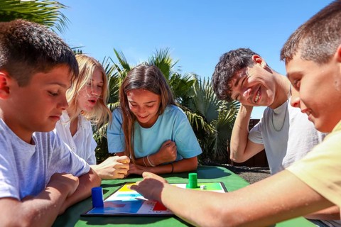 Two older siblings, a young man and woman, enjoy a board game outside with their younger triplets