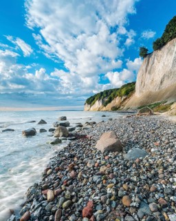 Chalk cliffs and rocky beach with boulders on the Baltic Sea under blue sky with cumulus clouds,