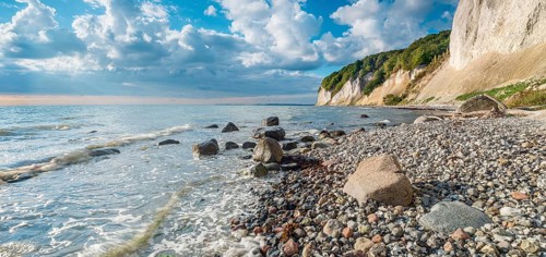 Chalk cliffs and rocky beach with boulders on the Baltic Sea under blue sky with cumulus clouds,