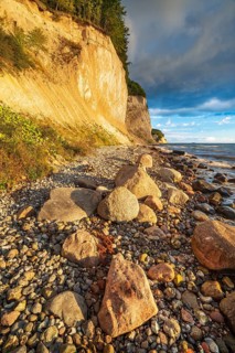 Chalk cliffs and rocky beach with boulders on the Baltic Sea in morning light under a blue sky with