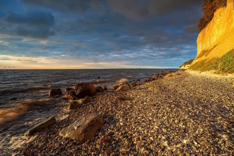 Chalk cliffs and rocky beach with boulders on the Baltic Sea in morning light under dark sky with