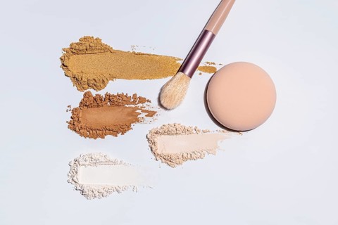 Top view of colorful, assorted face powders and a cosmetic brush on a light surface, showcasing