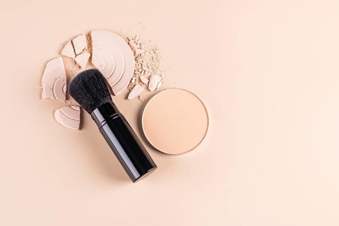 Top view of a makeup brush alongside a compact face powder and broken pieces of a loose powder