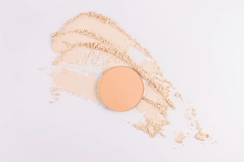 Top view of a circular compact powder alongside scattered loose face powder on a clean, white