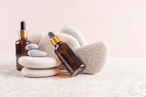 Two amber glass serum bottles with golden caps are artfully displayed among smooth gray stones,