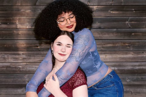 Two young Gen Z women, one Hispanic with curly hair, and the other of unspecified ethnicity, share
