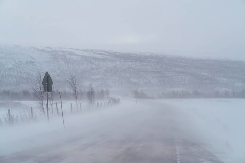 A blizzard envelops a remote road in Swedish Lapland, obscuring distant snow-covered hills and