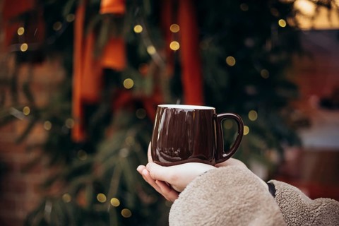 Cropped unrecognizable young woman holding a warm coffee mug in front of a beautifully decorated