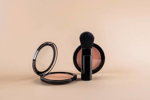 Open compact powder alongside a professional makeup brush, creatively arranged against a soft beige