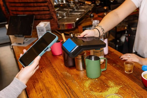 A customer uses a smartphone for contactless payment at a trendy specialty coffee shop, showcasing